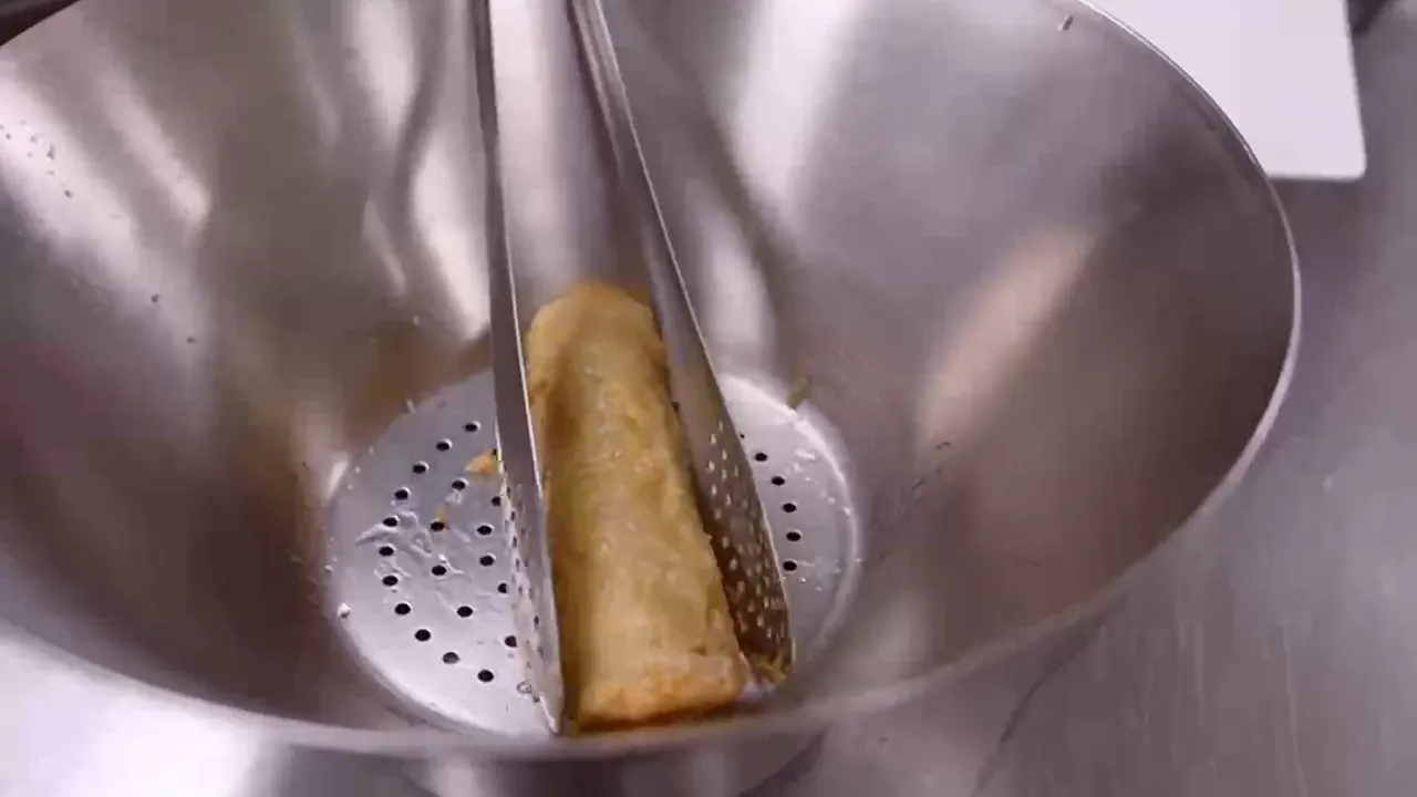 Een goudbruine loempia die met een tang uit de frituur komt.