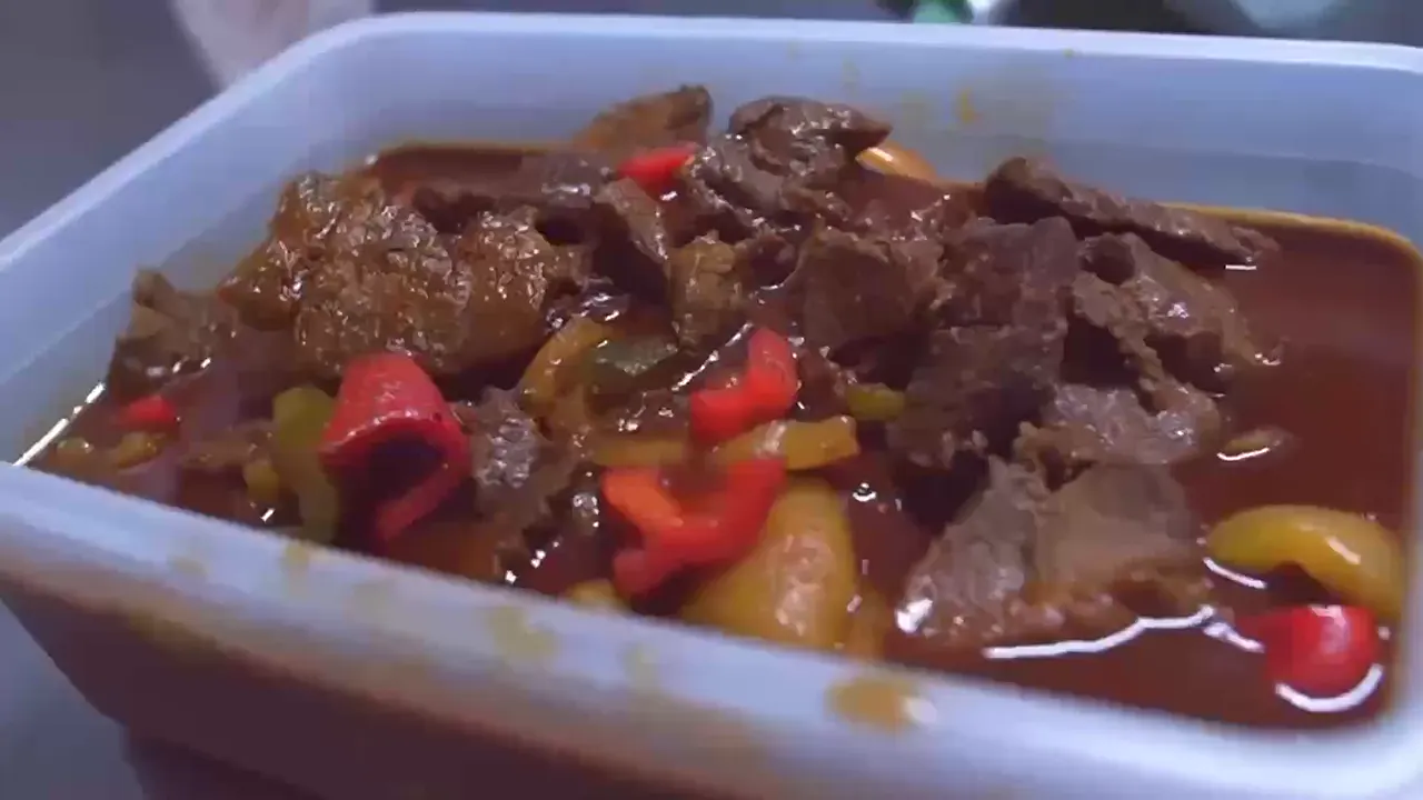 Een bak gestoofd rundvlees met rode en gele paprika in saus.