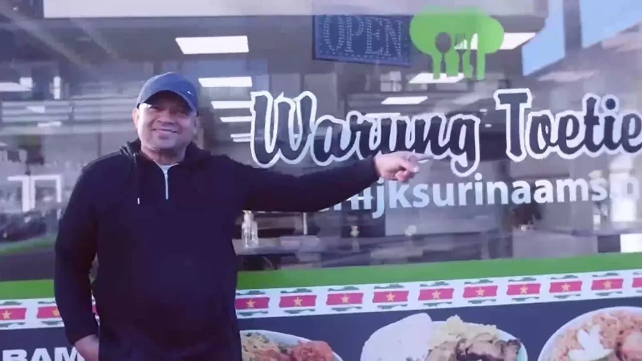 De eigenaar wijst lachend naar de naam Warung Toetie op het raam van de zaak.